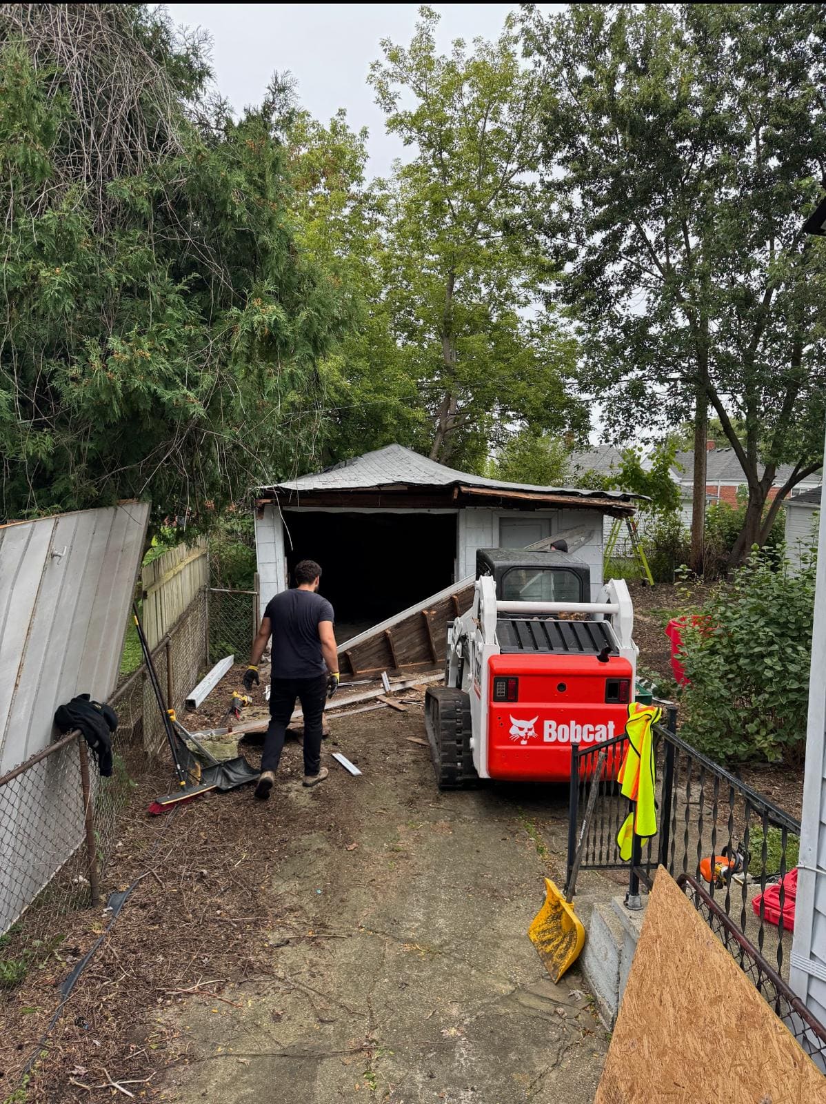 Crew member and a Bobcat skid steer during a garage demolition in a Metro Detroit backyard